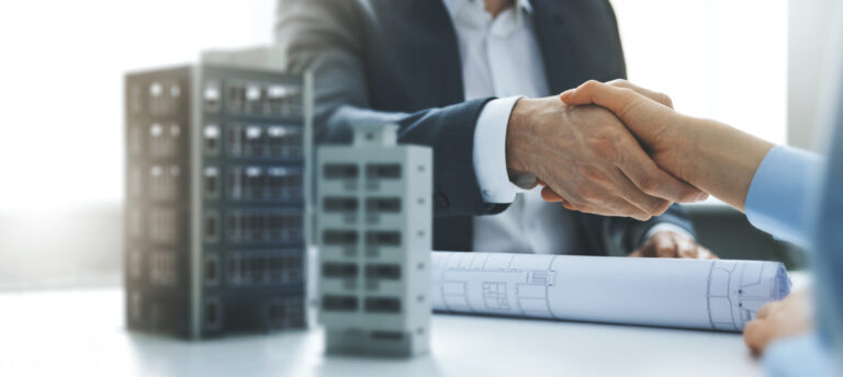 Two professionals shaking hands across a conference table with architectural plans